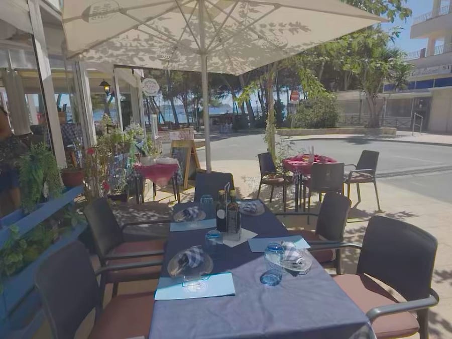 Tavoli apparecchiati sulla terrazza sotto l ombrellone, con il mare e i pini che si intravedono sullo sfondo fra gli alberi