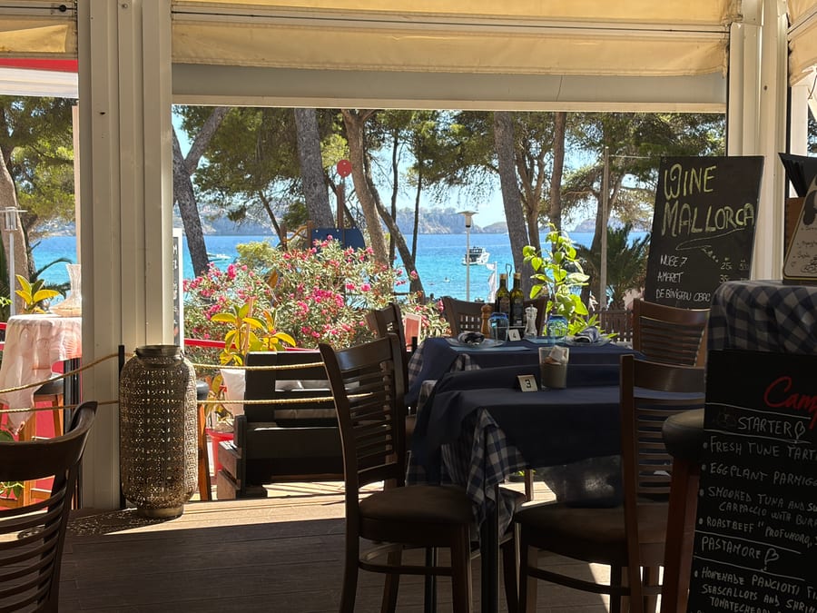 La vista dall interno del locale verso il mare: in primo piano due tavoli apparecchiati con tovaglie blu e a quadretti, numerati, con bottiglie d olio